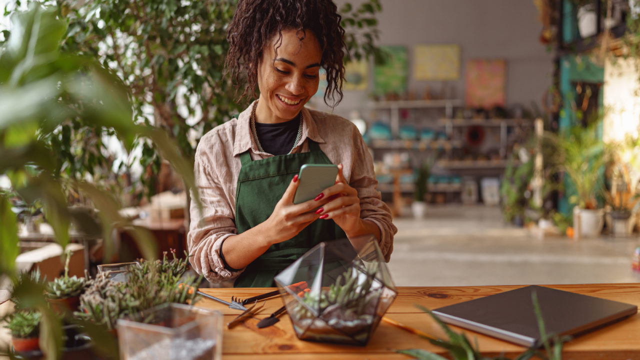 Smiling woman florist taking picture with her plants for publishing in social media